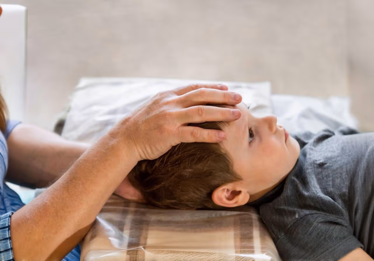 bambino visitato da un osteopata. il palmo del dottore è sulla testa del bambino, che è disteso su un lettino